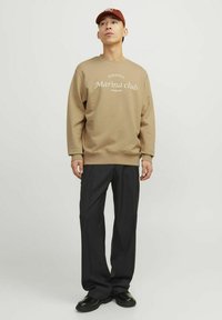 Khaki sweatshirt with text "Sardinia Marina club Premium," paired with black trousers and black shoes, creating a relaxed outfit.