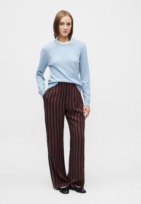 Hellblauer Strickpullover mit rundem Ausschnitt, kombiniert mit weitem Hosenbein und vertikalen roten und schwarzen Streifen. Glatte Textur, lässige Passform.