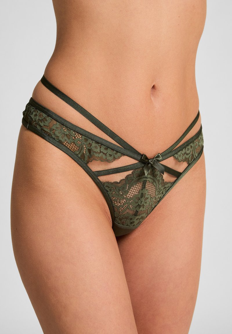 Olijfgroen kanten string met dubbele bandontwerp, versierd met bloemmotieven en een centrale strikdetail. Zachte, delicate textuur.