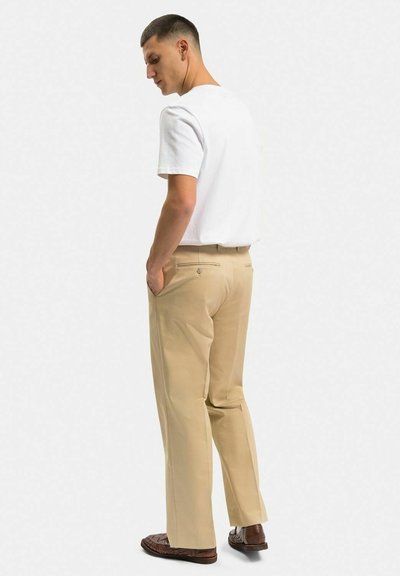 Beige sedanbyxor i rak passform, tillverkade av mjukt tyg med midjeband och sidofickor, kombinerade med en vit t-shirt med kort ärm.