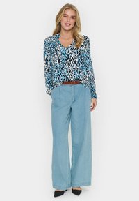 Långärmad blus med ett blått och svart leopardmönster, kombinerad med löst sittande ljusblå jeans och ett brunt bälte. Svarta skor fulländar outfiten.