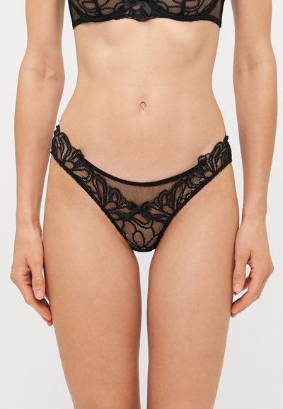 String noir en dentelle avec broderie florale, tissu transparent, bords festonnés et un petit nœud à l'avant de la ceinture.