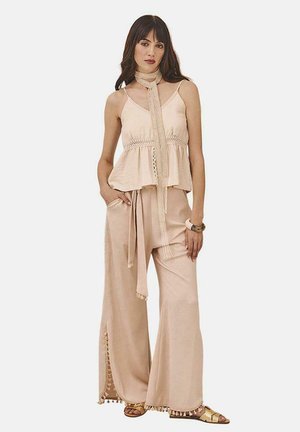 Top sin mangas de color beige claro con un dobladillo volátil y trenzado decorativo; pantalones de pierna ancha con aberturas laterales y acentos de borlas; combinados con sandalias.