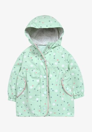 Veste de pluie vert clair avec des pois blancs, roses et gris. Elle dispose d'une capuche, d'une fermeture à pression et de deux poches avant aux bords arrondis.