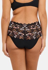 Slip in pizzo nero con ricami floreali in rosa e beige. La vita ha un bordo a forma di scallop e offre una finitura morbida e strutturata.