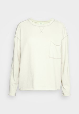 Kremowa bluza z długim rękawem, z okrągłym dekoltem i kieszenią na piersi, z widocznymi przeszyciami i luźnym krojem.