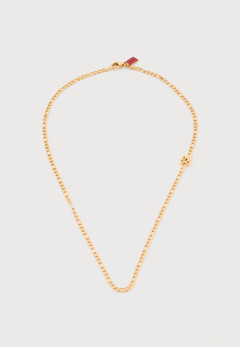 Κολιέ με αλυσίδα από χρυσό και μικρό μενταγιόν σε σχήμα τετράφυλλου τριφυλλιού με κούμπωμα καβουράκι σε ανοιχτό γκρι φόντο.