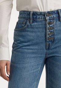 Blå denim jeans med høy midje, knappestolpe, fem knapper og tradisjonelle lommer. Stoffet har en lett tekstur.