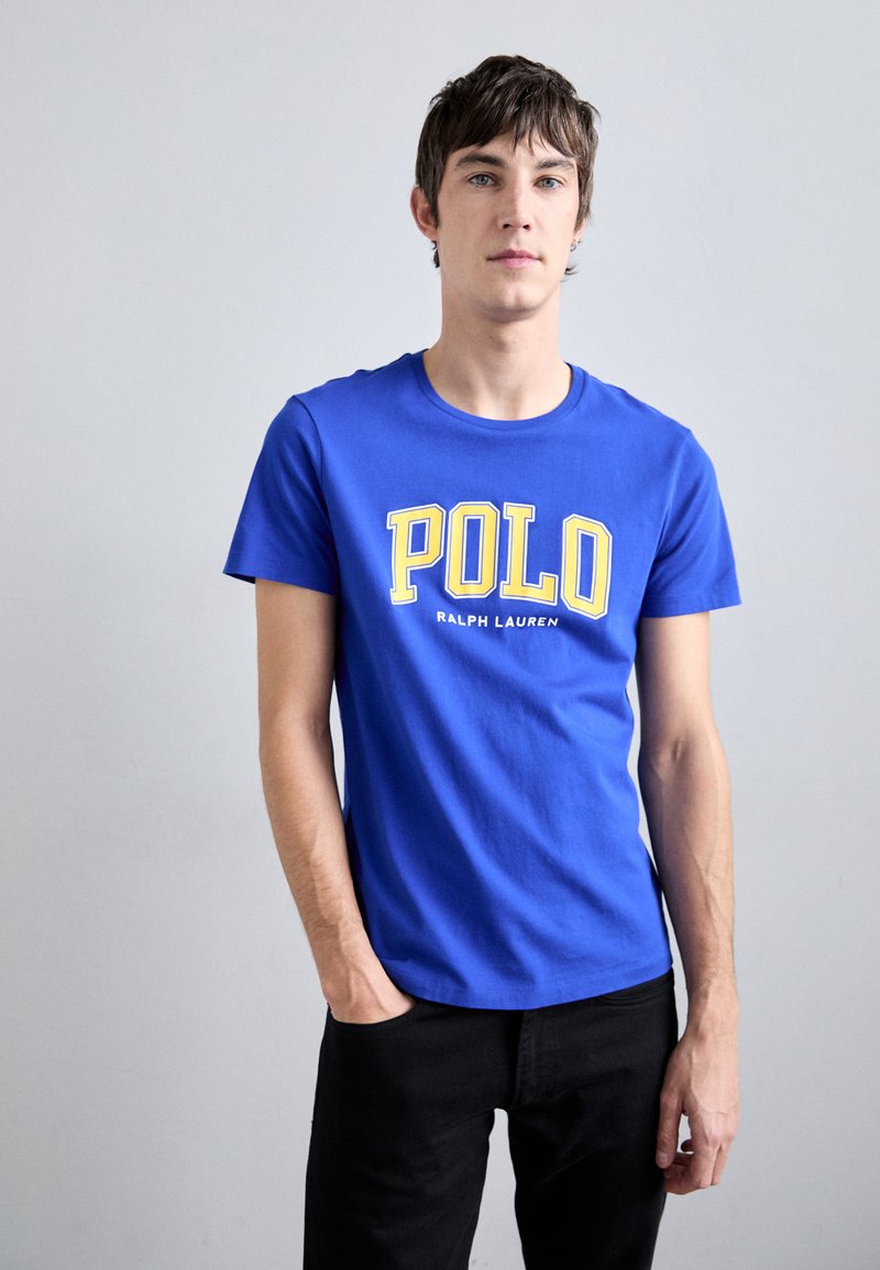 Camiseta de algodón azul con grandes letras amarillas "POLO" y "RALPH LAUREN" debajo, con cuello redondo y mangas cortas.