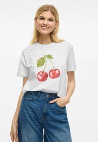 T-shirt blanc à manches courtes avec un graphisme de deux cerises rouges et des feuilles vertes. Le tissu semble doux et la coupe est décontractée.