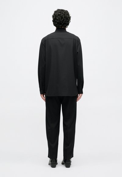 Melnā ar garām piedurknēm krekls ar taisnu piegriezumu, mīksts audums, aizmugurējā yoke šuve, kopā ar atbilstošām brīvā piegriezuma biksēm un melniem apaviem.