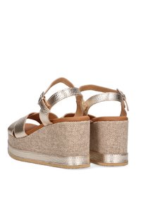 Sandalias de plataforma en tono dorado con textura de yute beige trenzada, que cuentan con correas anchas y un detalle metálico en el tacón. Cierre de hebilla en el tobillo.