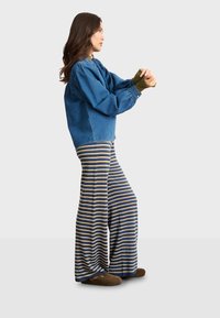 Jeansjacke mit Puffyärmeln, olivgrünen Manschetten, gestreiften, weit geschnittenen Hosen in Blau und Gelb sowie braunen Pantoletten.