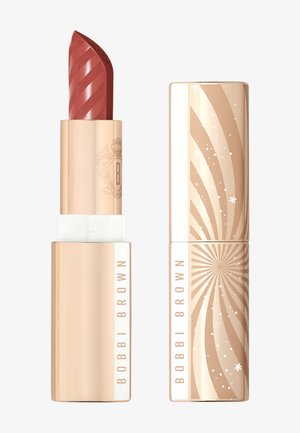Rouge à lèvres d'une teinte rouge-rose avec un design torsadé. Emballé dans un tube doré avec des motifs linéaires et d'éclatement. L'étiquette indique "Bobbi Brown."