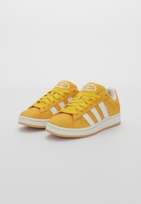 Yellow suede sneakers with white three-stripe design, round toe, cushioned collar, and rubber sole. Laces match the shoe color.