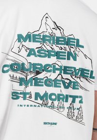 Witte katoenen t-shirt met een bergillustratie en groene tekst. De tekst bevat namen van skiresorts en het merk "SIXTH JUNE" in kleine letters.