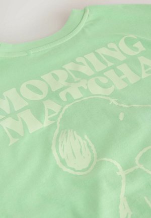 Šviesiai žalias medvilninis marškinėlis su dideliais, ryškiais baltais žodžiais "MORNING MATCHA" ir paprastu grafiniu dizainu. Minkšta tekstūra.