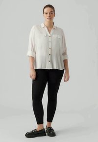 White button-up shirt with two chest pockets, rolled sleeves, and wooden buttons, paired with black leggings and chunky black shoes.