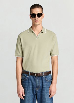 Khakifarbenes Poloshirt mit strukturierter Oberfläche, weißem Kragen und Ärmelakzenten, kombiniert mit blauen Jeans und braunem Gürtel. Schwarze Sonnenbrille getragen.