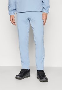 Világoskék, slim-fit nadrág, amely textúrált anyagból készült, fekete, masszív túracipőkkel párosítva, amelyek strapabíró talppal és fűzővel rendelkeznek.