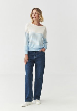 Pull léger avec des rayures horizontales bleu clair et bleu foncé, col bateau, associé à un jean bleu taille haute et des baskets blanches.