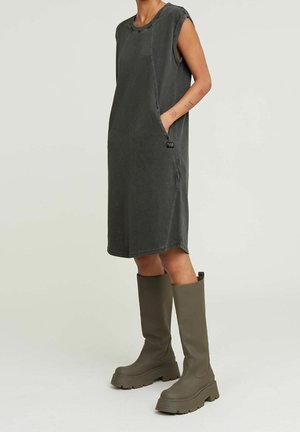 Robe sans manches gris foncé longueur genou avec poches latérales portée avec des bottes épaisses mi-mollet vert olive sur le mannequin.