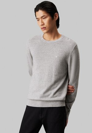 Sudadera de punto gris con escote redondo, puños y dobladillo acanalados, y pequeño logo blanco en el pecho; textura suave y corte casual.