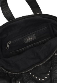 Zwarte leren tas interieur met een ritsvak, stoffen voering en een zichtbare label. Kenmerkt zich door studs aan de buitenkant.