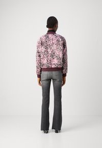 Bloemige bomberjack in roze en zwart, met ribgebreide boorden en kraag. Gecombineerd met grijze flared jeans, met rafelige zoom.