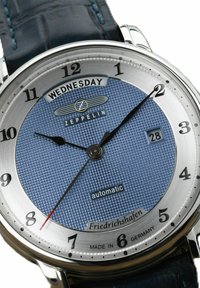 Analog-Uhr mit blauem strukturiertem Zifferblatt, Edelstahlgehäuse, schwarzen Zeigern, Datumsfenster auf 6 Uhr und dunkelblauem Lederarmband.