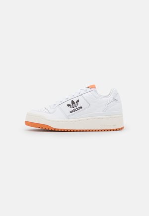 Witte Adidas lage sneaker met zwart logo, oranje zool en detail op de tong, zijstiksels en veters aan de voorkant.