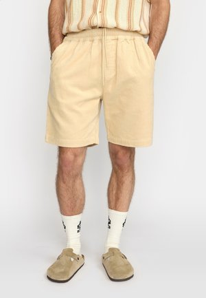 Beige corduroy shorts met een elastische tailleband, zijzakken en een casual pasvorm, gecombineerd met witte sokken en beige instap schoenen.