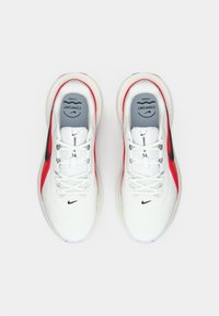 Λευκά αθλητικά παπούτσια με κόκκινες λεπτομέρειες και μαύρο λογότυπο. Μάσκα από διχτυωτό υλικό με υφασματική υφή. Λεπτές κορδόνες και επενδεδυμένος λαιμός για άνεση.