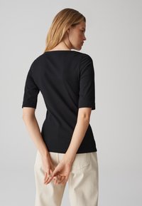 Schwarzes, figurbetontes T-Shirt mit kurzen Ärmeln, glatter Textur und quadratischem Ausschnitt, kombiniert mit hellen Hosen. Nur Rückansicht.