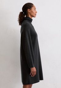 Czarna sukienka typu golf z miękkiego materiału, w kształcie A, z długimi rękawami, ściągaczami na mankietach i gładką fakturą, sięgająca do połowy uda.