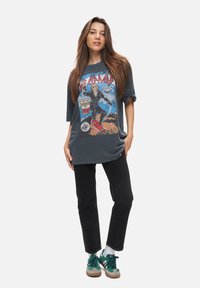 Grafisk T-shirt i kolfärgad med en färgglad banddesign, avslappnad passform, uppvikta ärmar, tillsammans med svarta jeans och gröna sneakers.