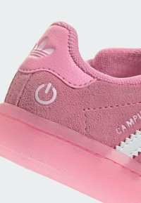 Pink suede sneaker featuring a rubber sole, textured accents, and white branding. Rounded design with tonal stitching and power icon detail.