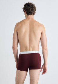 Bordó boxer alsónemű, fehér derékrésszel, a "Calvin Klein" logóval. Sima anyag, szoros szabás, hátulról nézve.