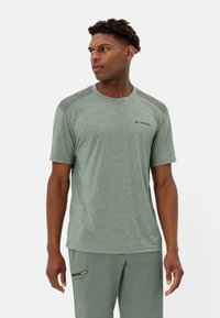 Maglietta atletica verde con maniche corte, tessuto testurizzato, dettagli grigi sulle spalle e logo sul petto, abbinata a pantaloni coordinati.