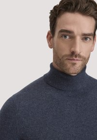 Navyblauer, gerippter Rollkragenpullover aus weichem Stoff, mit einer figurbetonten Silhouette und einem hohen Kragen, gezeigt am Oberkörper eines Models.