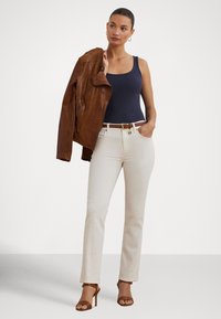 Top azul-marinho, casaco de couro castanho, jeans brancos de corte reto, cinto castanho com detalhe dourado e sandálias castanhas de salto. Conjunto simples e casual.