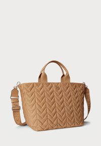 Quilted tan tote bag with chevron pattern, dual handles, adjustable strap, and logo embellishment. Matte finish with soft texture.