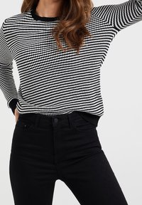 Maglione con motivo in bianco e nero, collo rotondo, maniche lunghe e polsini a coste, abbinato a jeans neri a vita alta.