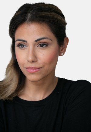 Porträt einer Person mit mittelbrauner Haut und dunklen, glatten Haaren, die ein schwarzes Shirt trägt. Subtile Schminke betont die natürlichen Merkmale.
