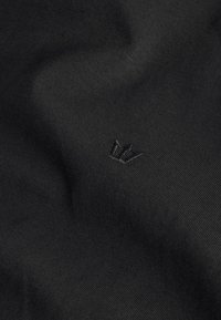 Black fabric with subtle embroidered crown logo centered, showing fine ribbed texture and gentle folds.