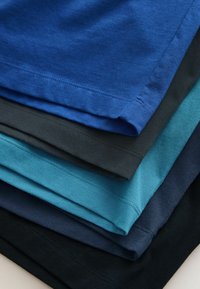 Stack of folded T-shirts in various blue shades, showing the hem and stitching details on each garment.
