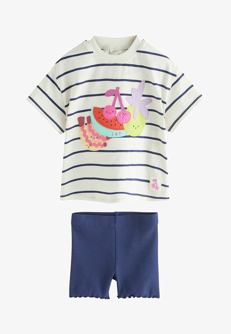 Camisa blanca de manga corta con rayas marinas y parches de frutas sonrientes de colores, combinada con pantalones cortos de canalé en azul marino sólido con dobladillos ondulados.