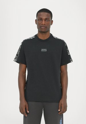 Black cotton t-shirt with short sleeves featuring patterned fabric on the shoulders and a small logo patch on the chest.
