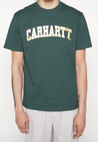 Zielony bawełniany T-shirt z dużym, okrągłym, złotym logo "CARHARTT" na klatce piersiowej. Krótkie rękawy i okrągły dekolt.