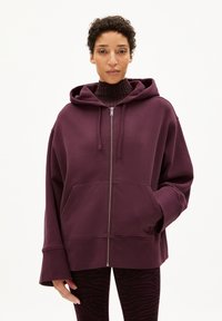Bordeaux zip-up hoodie met een capuchon, grote frontzakken en brede mouwen, gecombineerd met zwarte leggings met een zebra patroon.
